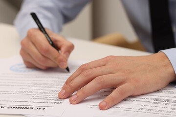 Man signing licensing agreement document at table indoors, closeup