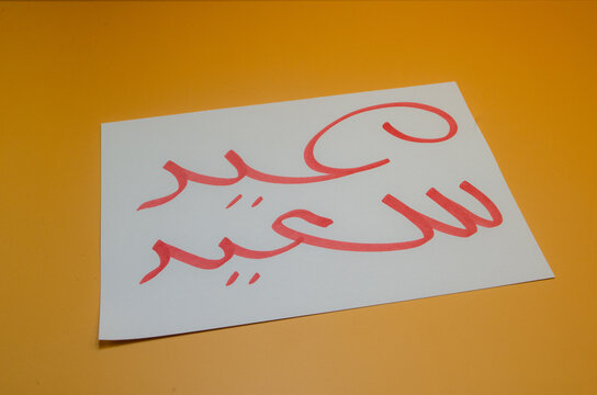 A heartfelt Eid greeting written in elegant red calligraphy on a simple white card against a warm orange background.