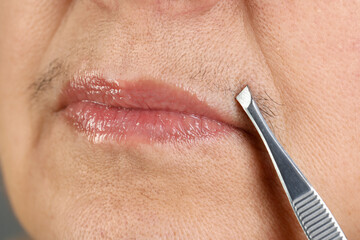 Senior woman plucking her mustache with tweezers, closeup