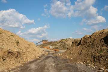 Aged industrial ruins featuring a deteriorating stone crusher, forgotten machines, and scattered sand, gravel, and rock heaps.