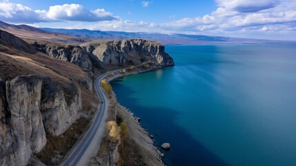 A high-angle aerial shot of a coastal road hugging the edge of a vibrant blue lake, dramatic cliffs rising on one side, relaxing tourism concept