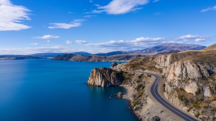 A high-angle aerial shot of a coastal road hugging the edge of a vibrant blue lake, dramatic cliffs rising on one side, relaxing tourism concept