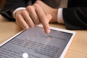 Electronic signature. Man using tablet at wooden table, closeup