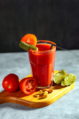 Vegetable shaken cocktail in glass on dark grey background. Red tomato cocktail. Served with tomatoes and pickles. Vegan menu.