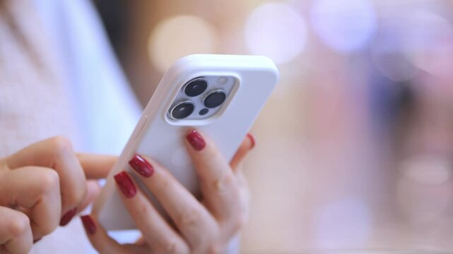 Woman is holding a white iPhone with a red nail polish on her nails. She is texting on the phone