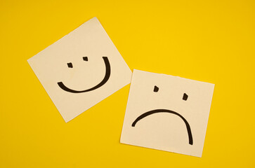 A simple contrast of happiness and sadness, depicted by hand-drawn smiley and frowny faces on white...