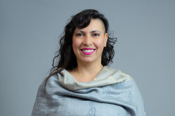 Cheerful woman with half-shaved hairstyle wearing a gray shawl, looking at camera with smile and approachable expression. Ideal for fashion, lifestyle, individuality, personal identity. Copy space.