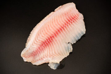 Fresh tilapia fillet on black background, top view.
