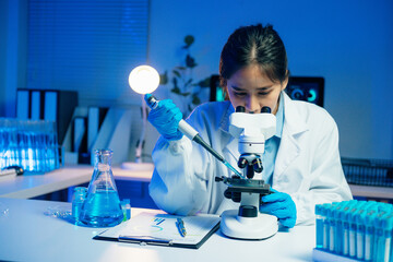 Asian scientist using micropipette and microscope during medical research in laboratory