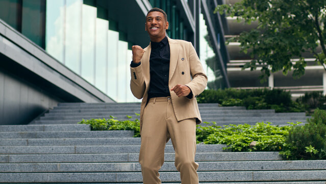 Happy successful excited fast running on office stairs building company walk African American man guy male businessman business in city celebrate achieve winner yes gesture champion opportunity win - Powered by Adobe