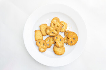 An array of butter cookies is arranged on a white plate, showcasing their variety and tempting texture against a clean backdrop.