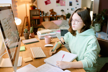 Portrait of teen girl with prosthetic arm gazing at computer screen while studying with focused...