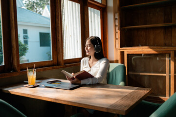 Young woman reading a book and listening to music in a cafe