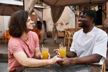 Two handsome men share a heartfelt moment over drinks at a cozy cafe on a sunny afternoon