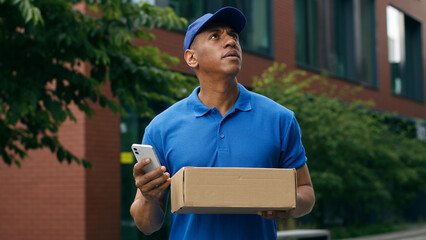 African American courier man confused look at mobile phone GPS map online searching location...