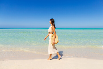 Side view of woman tourist with bag walking on tropical island, enjoying turquoise ocean water and...