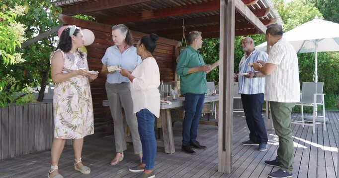 Diverse seniors enjoying in garden celebration, chatting and sharing food on wooden deck