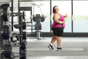 Fototapeta premium Corpulent woman in sportswear at a gym holding a bottle