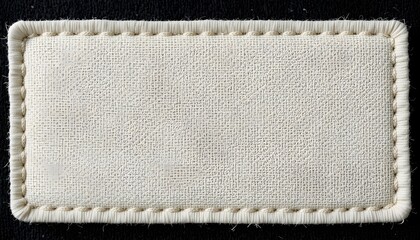 A close-up of an off-white fabric label that is blank and has a stitched border, set against a black backdrop