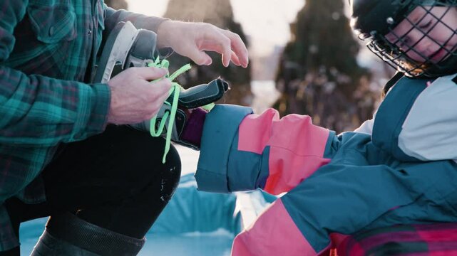 Dad lacing up skates for kid