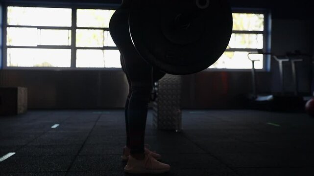 Low camera orbits woman in gym performing barbell deadlift exercise