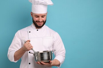 Happy confectioner in uniform holding whisk and cooking pot on light blue background