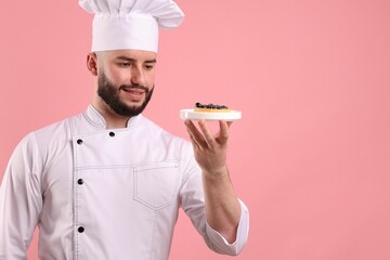 Happy confectioner in uniform holding tart with blueberries on pink background