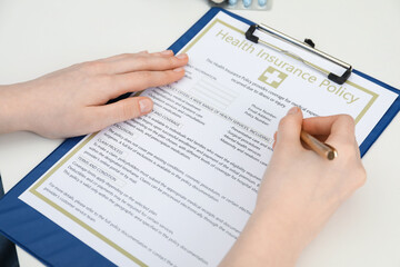 Obraz premium Doctor with pen filling out health insurance policy at white table, closeup