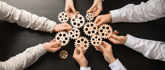 Hands holding wooden gears on dark wooden background, top view