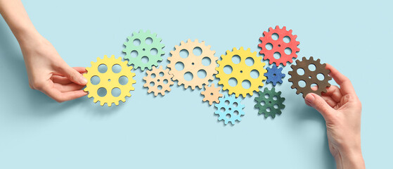Hands holding wooden gears on light blue background, top view