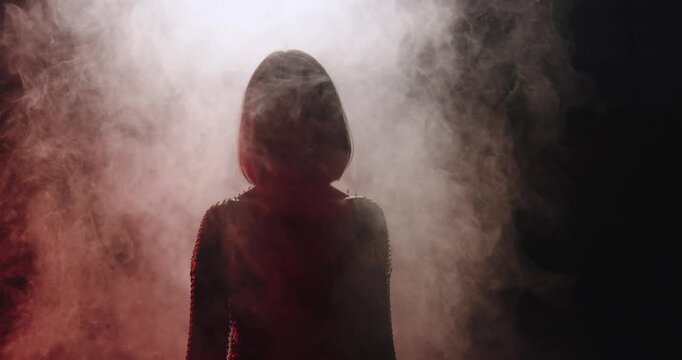 unknown woman walks out of fog, face is not recognizable, dark background