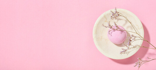 Bowl with bath bomb and dried flower on pink background