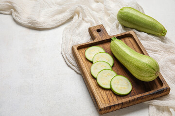 Wooden board with cut and whole zucchini on light background