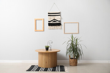 Wooden coffee table and houseplant near grey wall with macrame