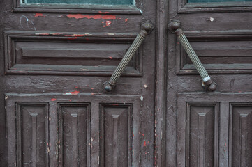 Weathered wooden door with antique metal handles shows signs of peeling paint and rustic charm