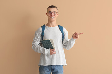 Happy male student in eyeglasses with notebooks pointing at something on beige background