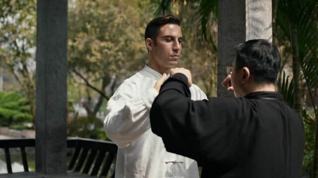 A young man practices Kung Fu with a master in a peaceful outdoor setting