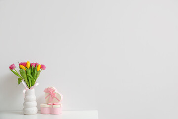 Vase with tulips and gift boxes on shelf near light wall. International Women's Day celebration