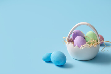 Ceramic basket with painted Easter eggs and paper strips on blue background
