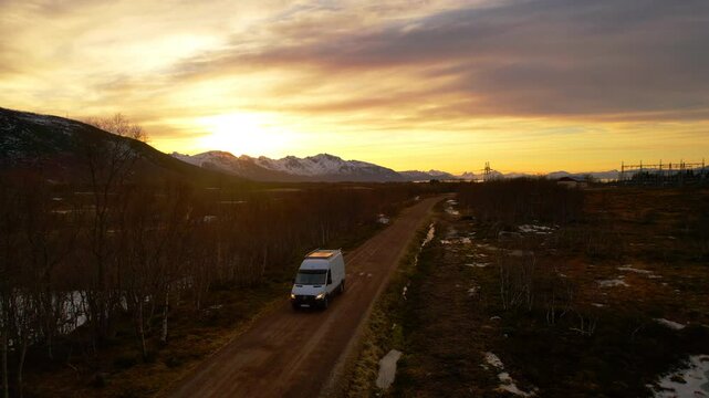 Aerial view of a van driving down a dirt road at sunset on an adventure in remote land with mountains and light snow cover