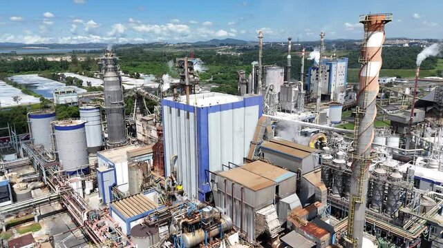 Imagem a&eacute;rea de ind&uacute;stria de papel e celulose com chamin&eacute;s e caldeiras em funcionamento. Fuma&ccedil;a e poluentes vis&iacute;veis, destacando o impacto ambiental da atividade industrial