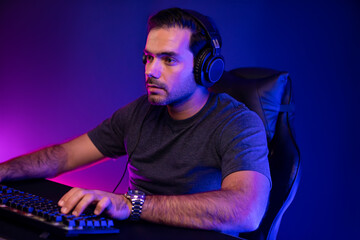 Smart gaming streamer concentrating gaming players trying to pass the level at mission completed, using headset and mic for communicate others on streaming live at neon lighting studio room. Surmise.