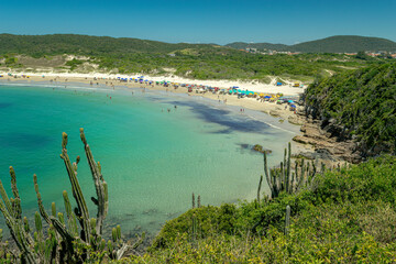 Naklejka premium View from above of part of Praia das Conchas. With crystal clear waters, many swimmers, rocks and mountains around. Cabo Frio, Rio de Janeiro, Brazil.