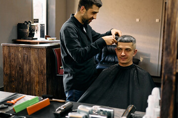 A hairdresser maneuvers scissors expertly while cutting a customer's hair in a modern barbershop. The atmosphere is vibrant and inviting, showcasing stylish decor and tools