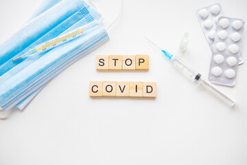 Obraz premium Medical supplies including a mask, syringe, thermometer, pills, and the phrase 'Stop COVID' formed with wooden blocks on a white background