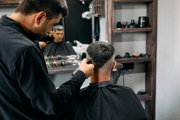 A skilled hairdresser is carefully cutting the hair of a client in a well-equipped barbershop. The atmosphere is professional, showcasing grooming tools and attention to detail in haircutting