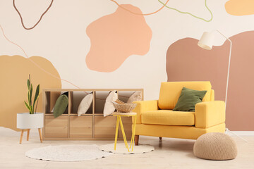 Cozy armchair, lamp and shelving unit with cushions in interior of living room