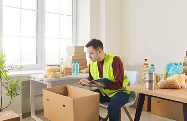 Young man volunteer sorting donations of foodstuffs in cardboard boxes for charity food drive. Male...