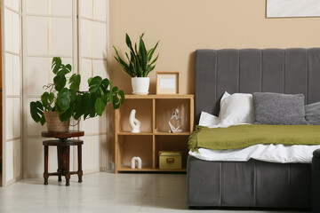 Interior of stylish bedroom with big bed, shelf unit and plants