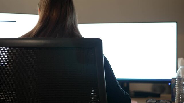 Woman Deep in Work on Modern PC Setup, Back View